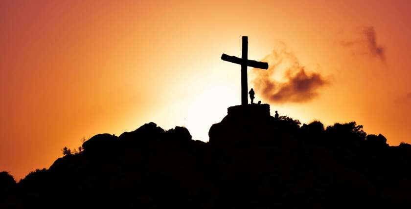 Majestic silhouette of a cross on a hill during a vivid sunset, symbolizing spirituality.